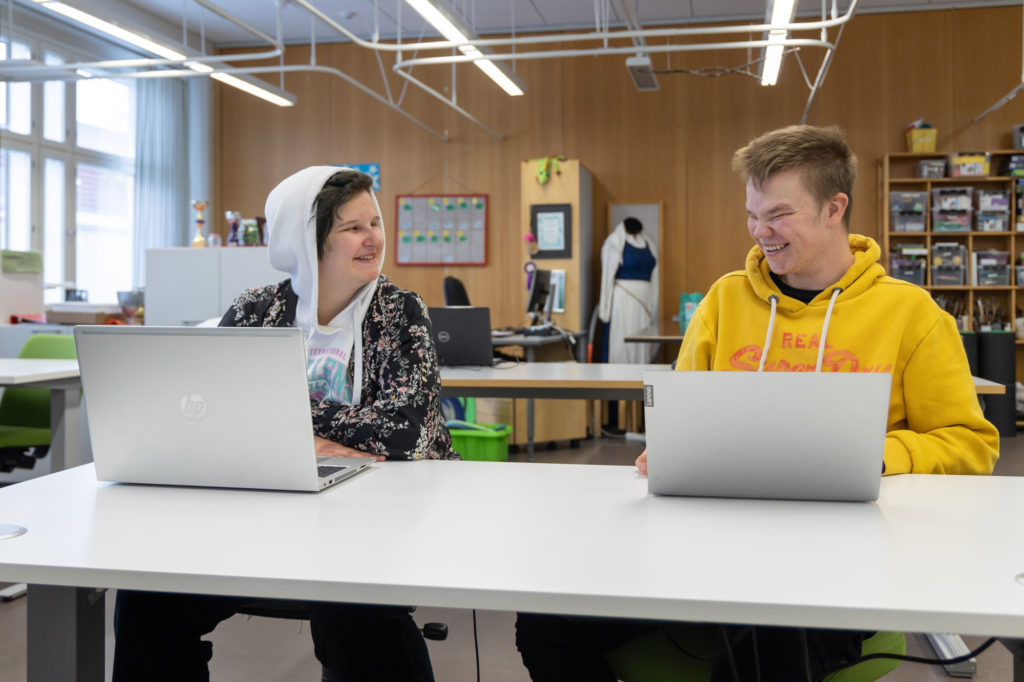 Kaksi opiskelijaa luokkatilassa kannettavien tietokoneiden äärellä.