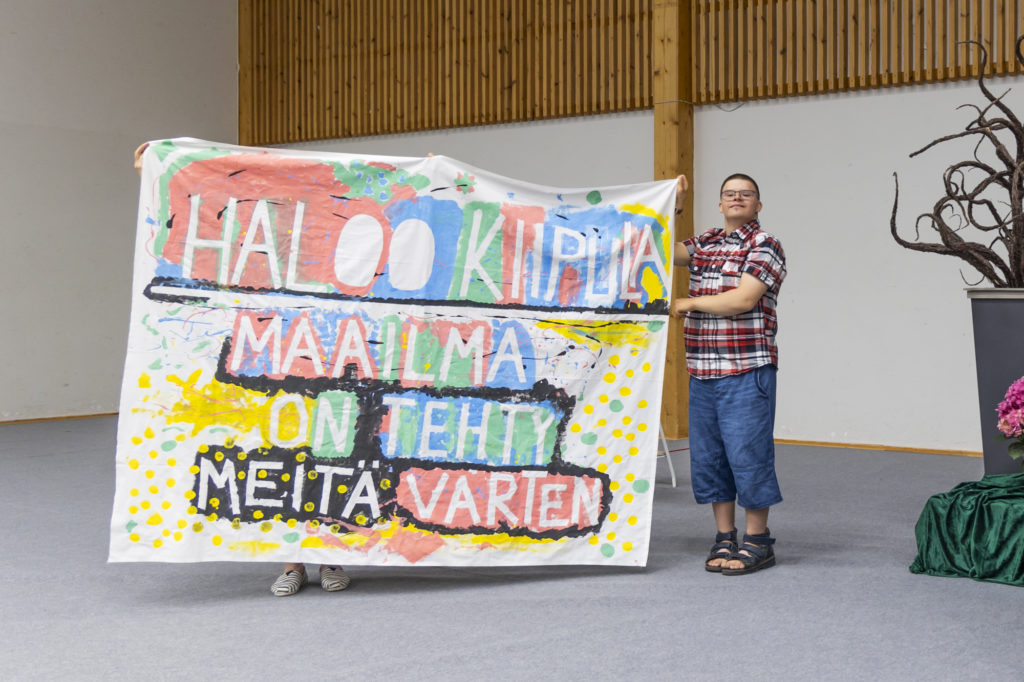 Telma-opiskelija pitelee lakanaa, jossa lukee "Haloo Kiipula, maailma on tehty meitä varten".