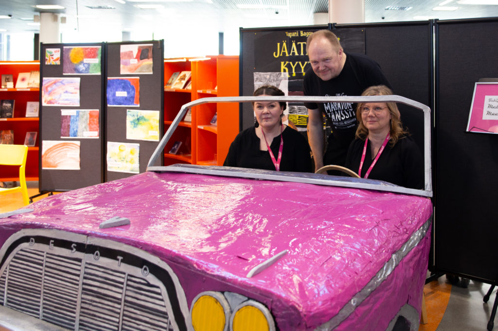 Ohjaaja Maria Nurminen, kirjailija Tapani Bagge ja opettaja Minna Saarinen opiskelijoiden tekemän rekvisiitta-auton takana.
